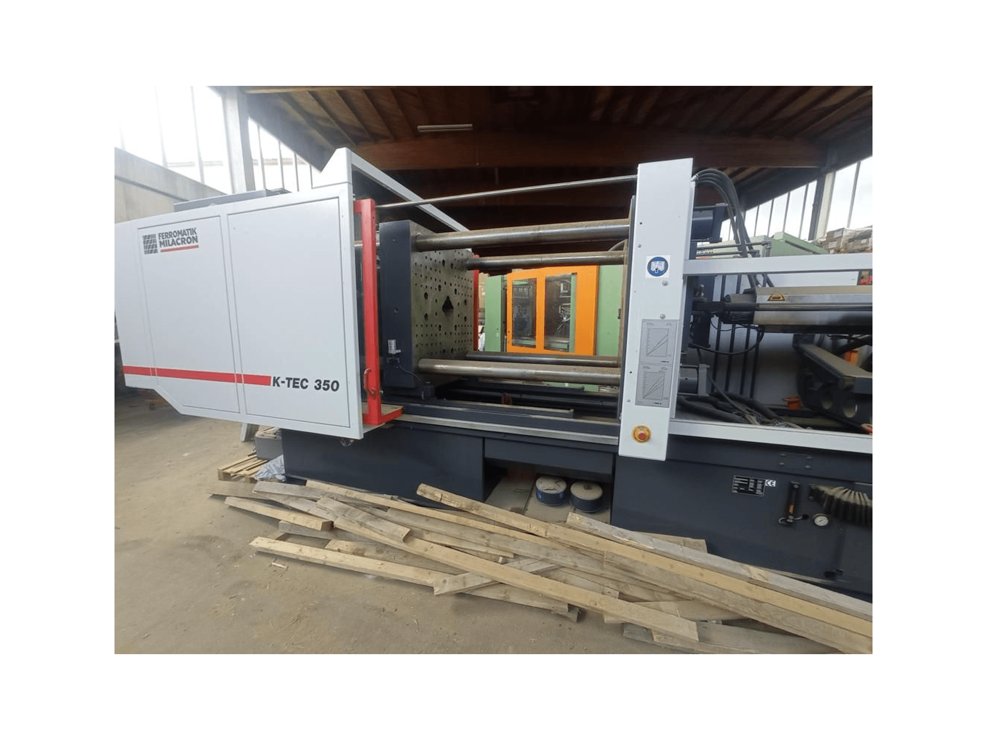 Ferromatik Milacron K-TEC 350, žiūrint iš šono, demonstruoja savo sudėtingus mechanizmus ir valdymo įtaisus.