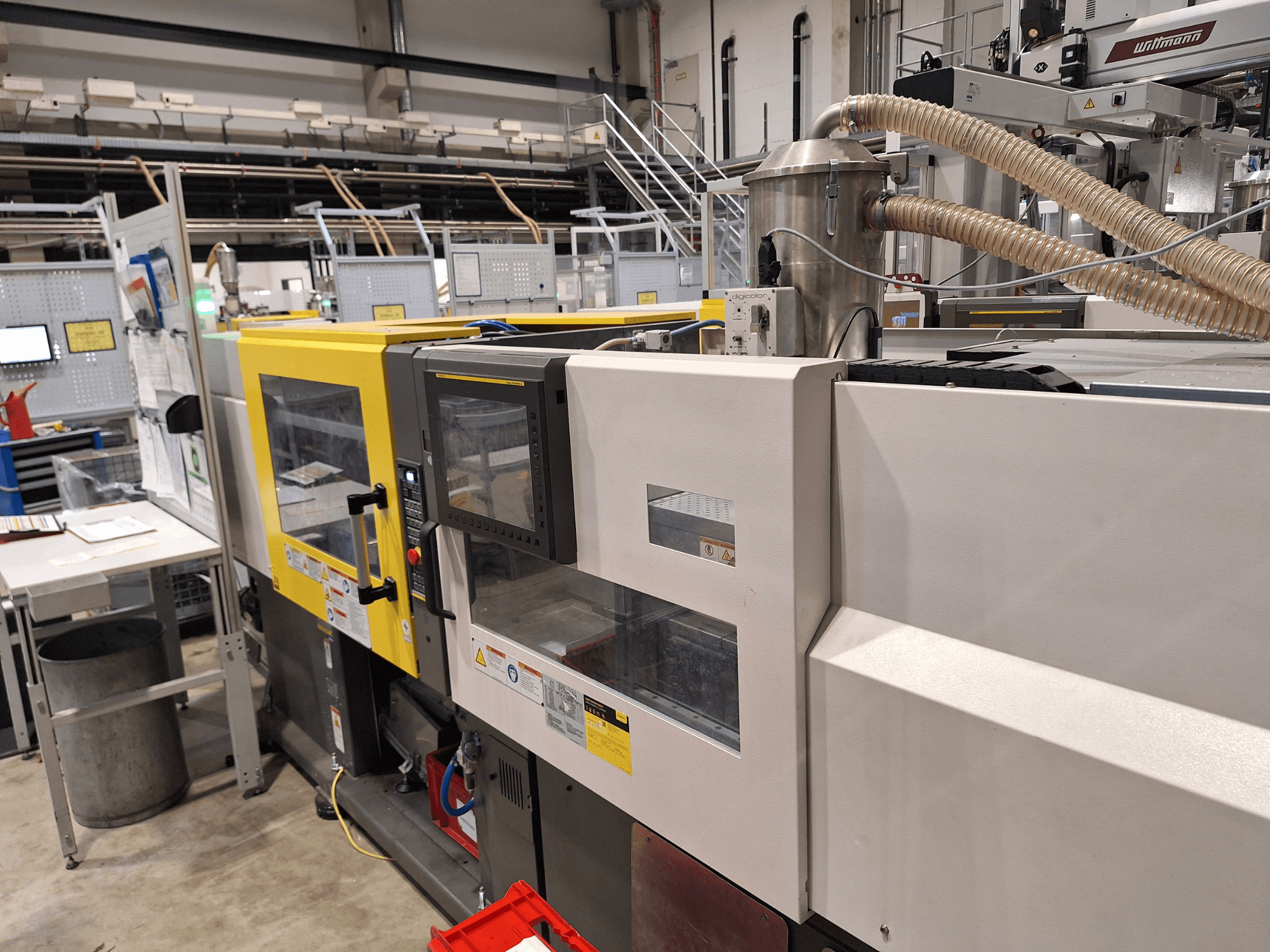 Įvairiaspalvės liejimo mašinos su geltonos ir pilkos spalvos sekcijomis, valdymo skydeliu ir išmetimo sistema vaizdas iš priekio.